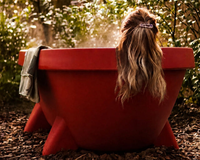 Vrouw ontspant in een terracotta Gardentub in een groene tuin.